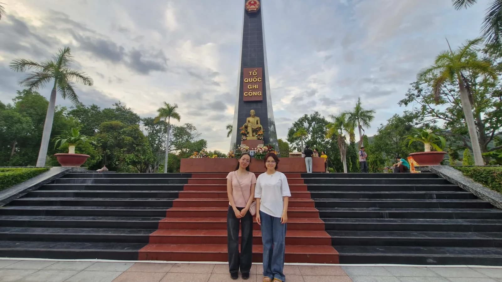 Hai bạn trẻ đứng trước đài tưởng niệm mang dòng chữ “Tổ quốc ghi công”.
