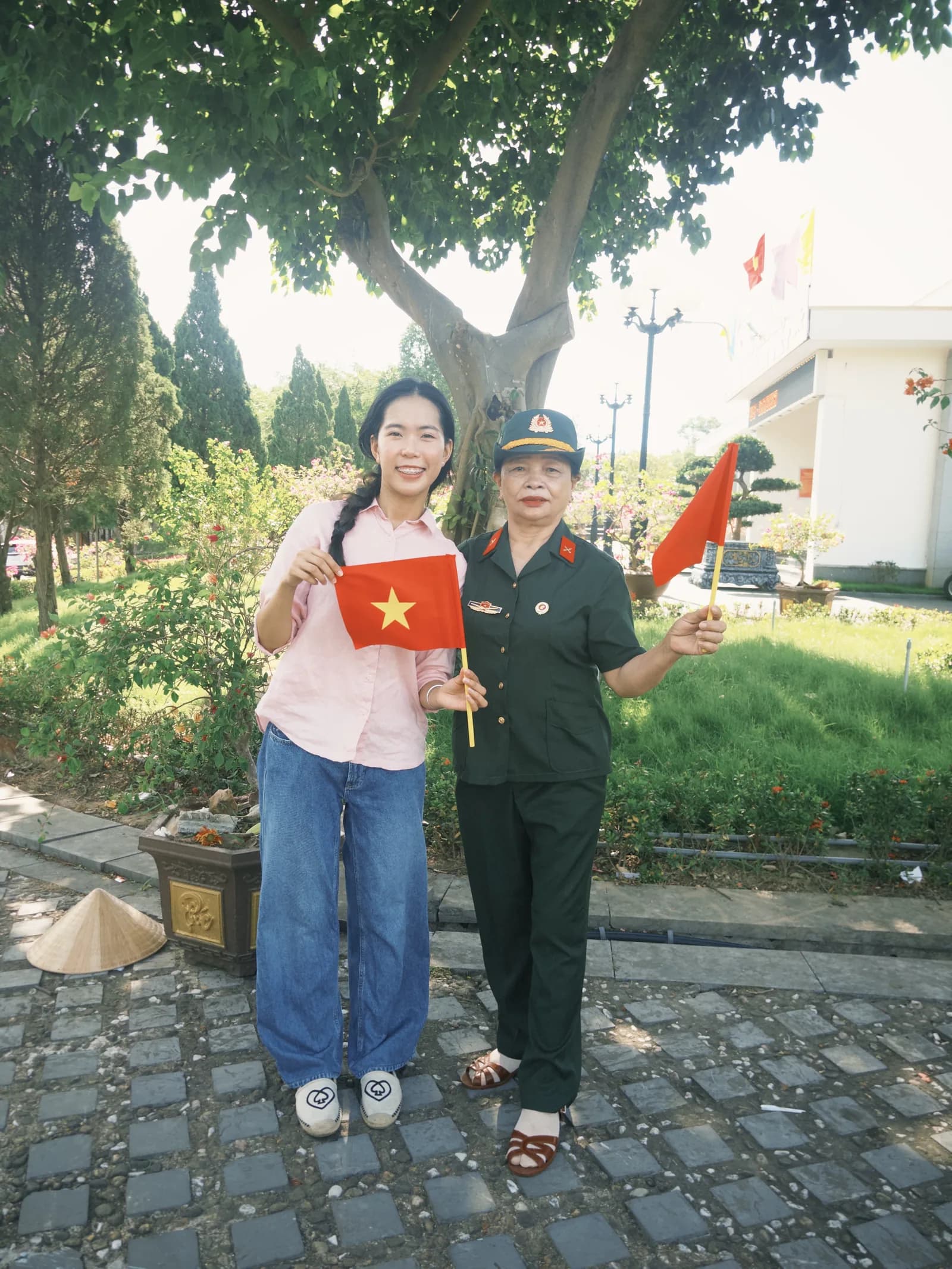 Một bạn trẻ và một nữ cựu chiến binh cùng cầm cờ Tổ quốc trong khuôn viên nghĩa trang.