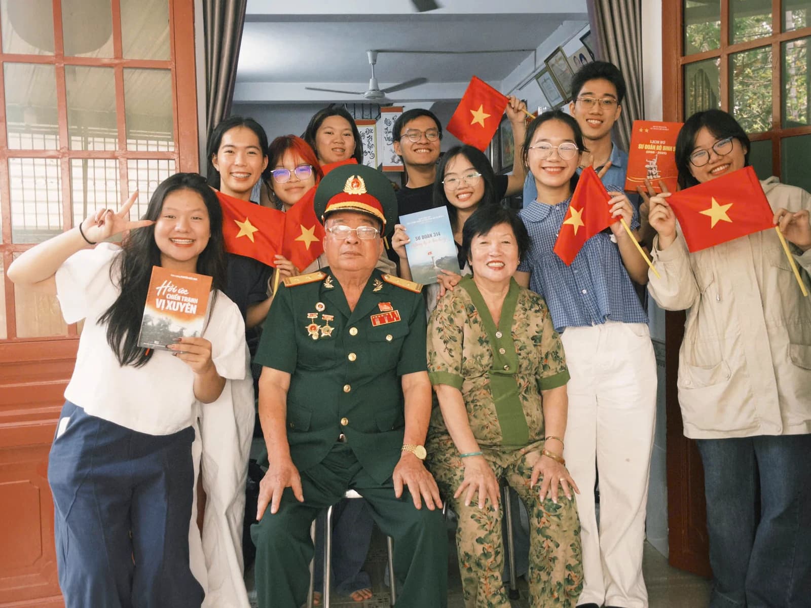 Một nhóm bạn trẻ chụp ảnh cùng hai cựu chiến binh, cầm cờ Tổ quốc.