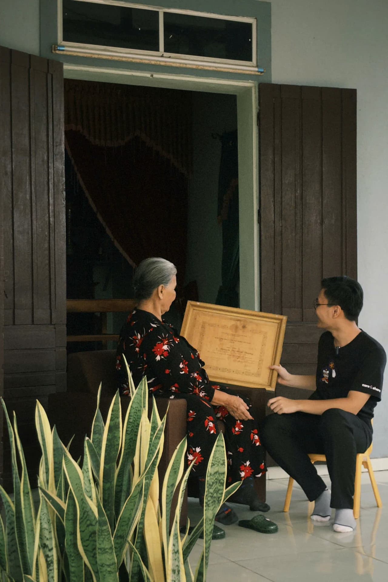 Một phụ nữ lớn tuổi và một bạn trẻ cùng xem một kỷ vật được đóng khung.
