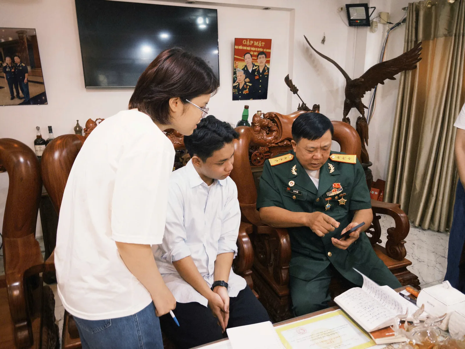 Hai bạn trẻ cùng một bác cựu chiến binh xem lại giấy tờ và hình ảnh cũ.