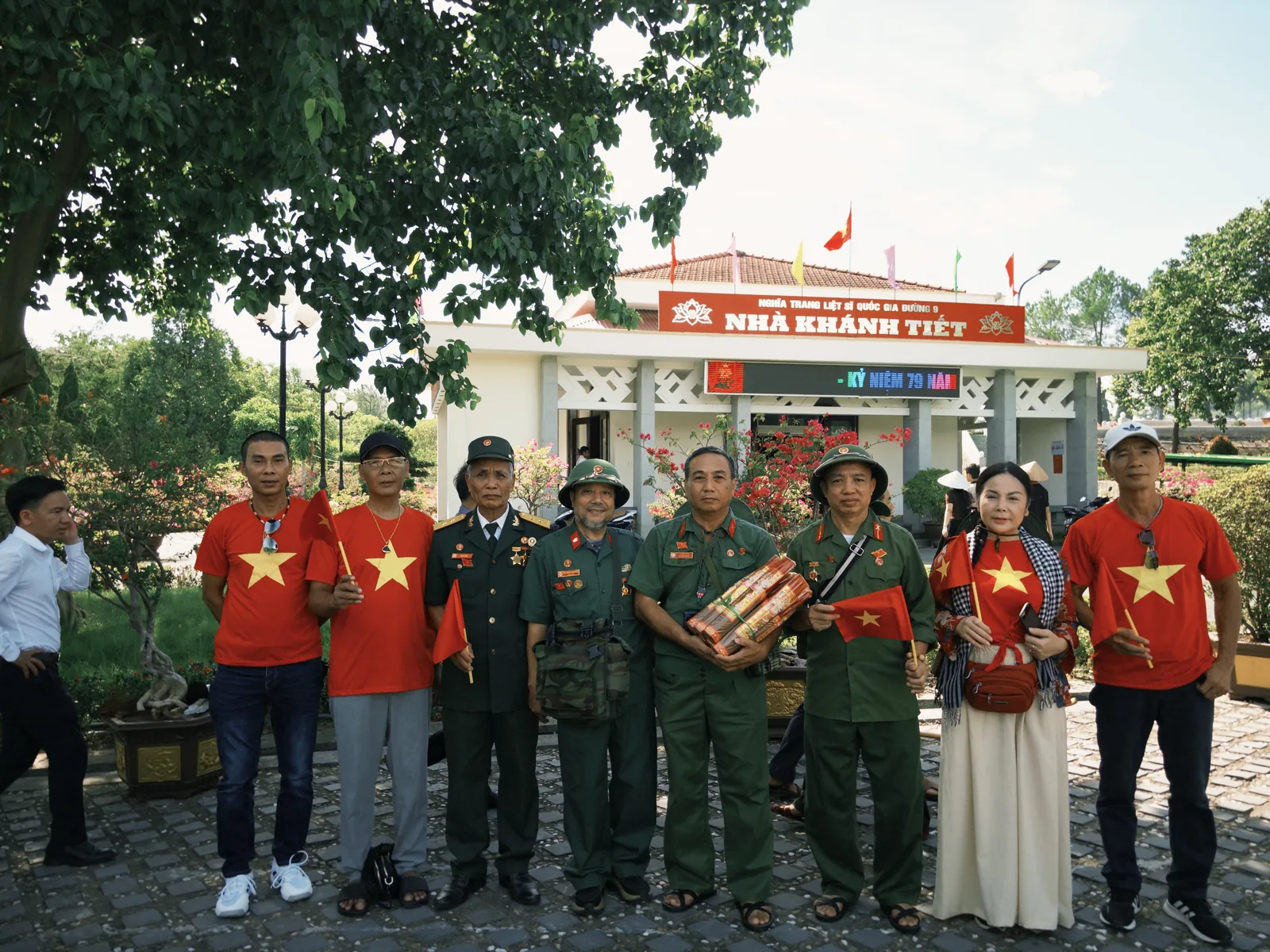 Các bác cựu chiến binh và người nhà lắng đứng trước Nhà khánh tiết, Nghĩa trang Liệt sĩ Quốc gia Đường 9, tay cầm cờ Tổ quốc và bó hương.