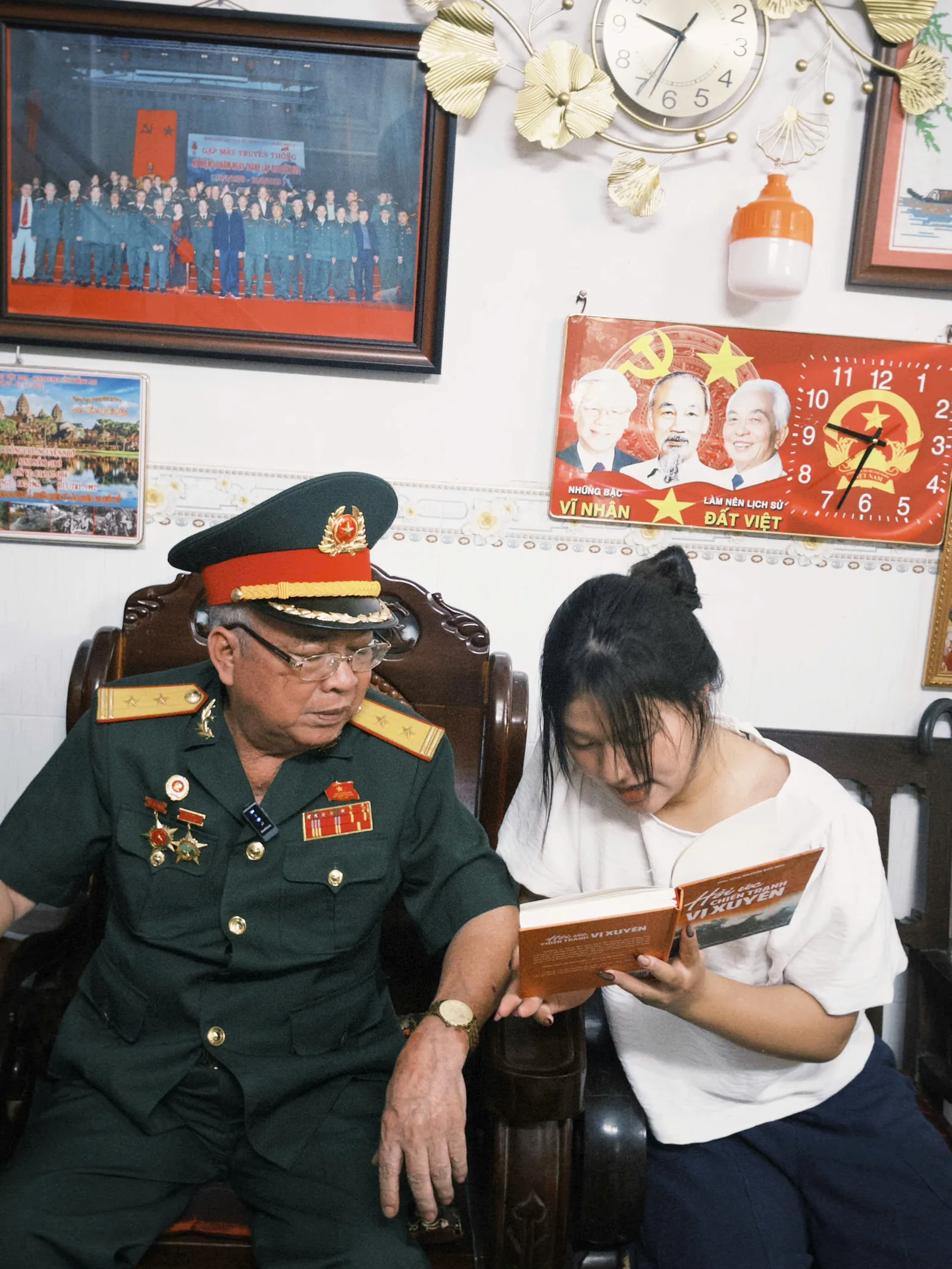 Một bác cựu chiến binh và một bạn trẻ cùng ngồi đọc một cuốn sách trong nhà bác.